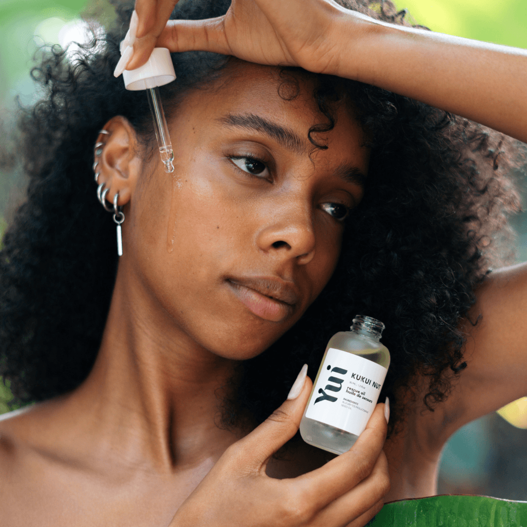 Vrouw brengt Kukui Nut Rescue Oil aan op haar gezicht.