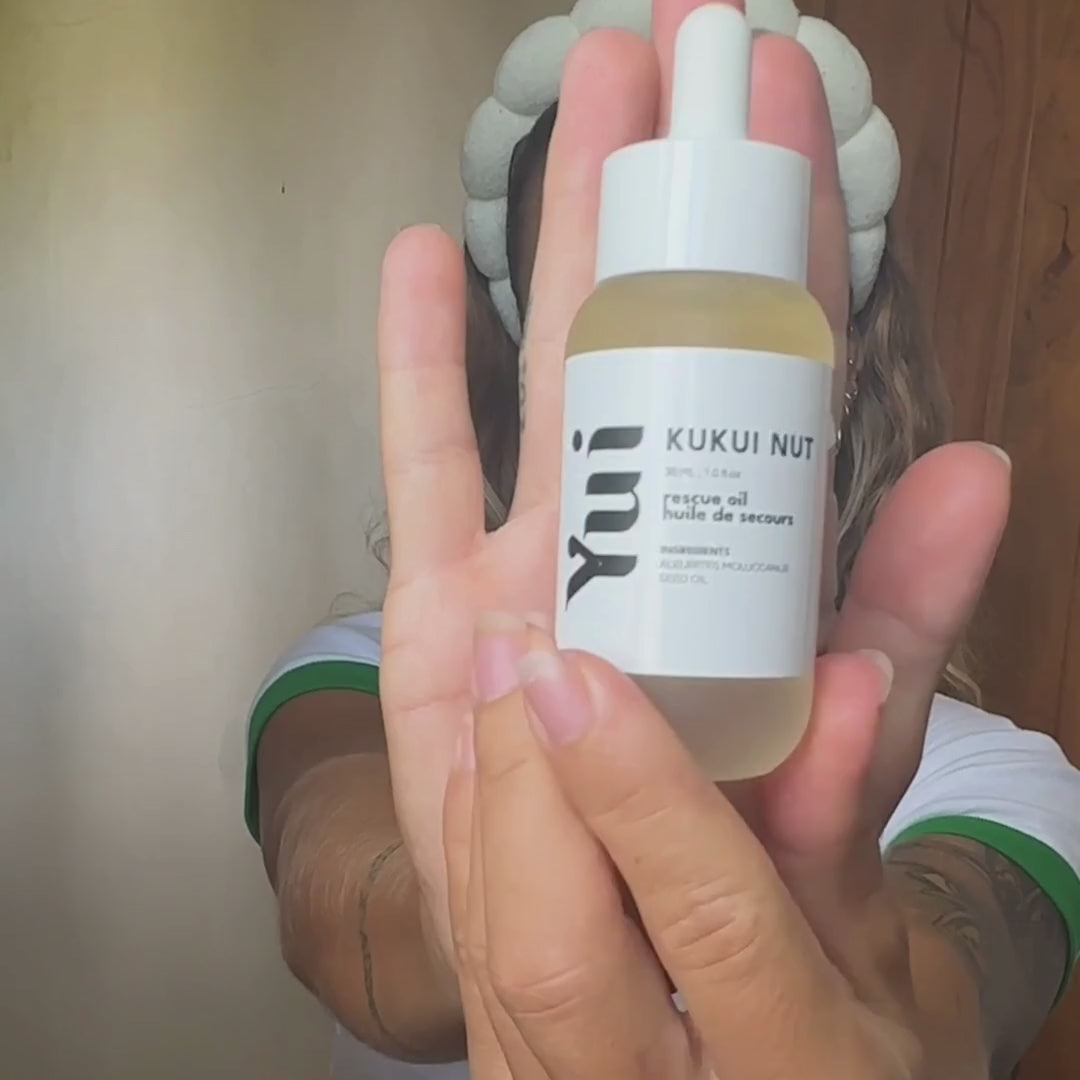 Persoon met flesje Kukui Nut Rescue Oil close-up.